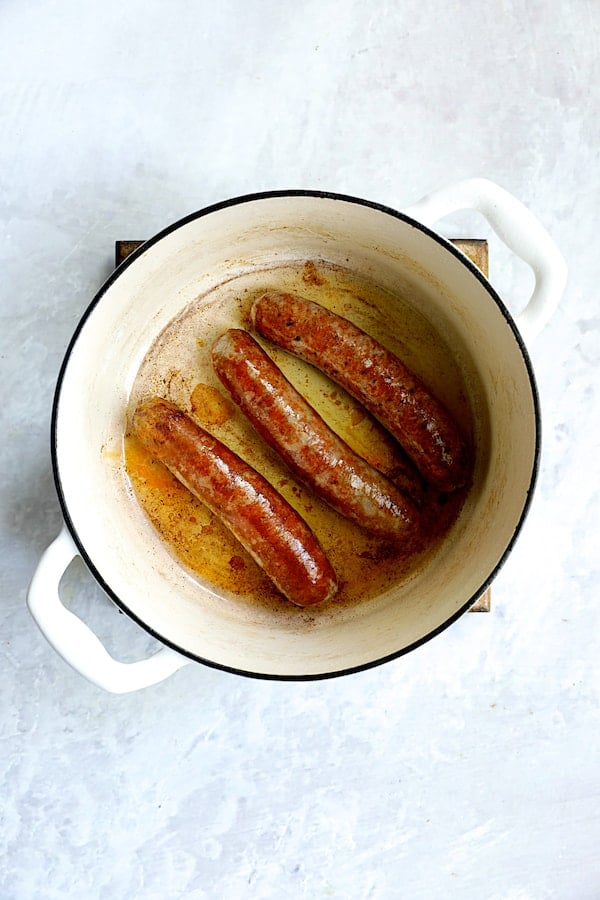 Photo of three links of chorizo being browned in white Dutch oven.