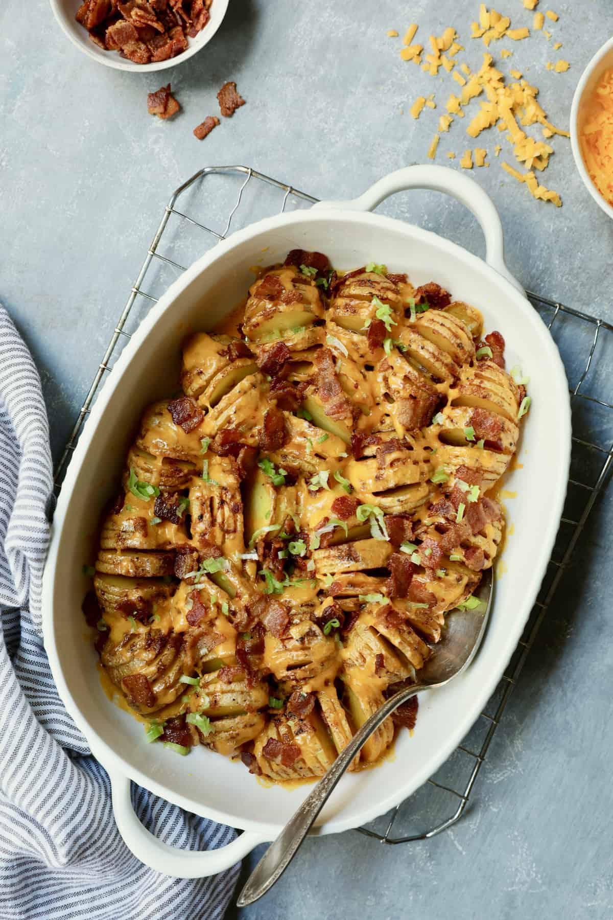 Photo of Baby Hasselback Potato Bake with Cheddar and Bacon on cooling rack with bacon and cheese scattered about.