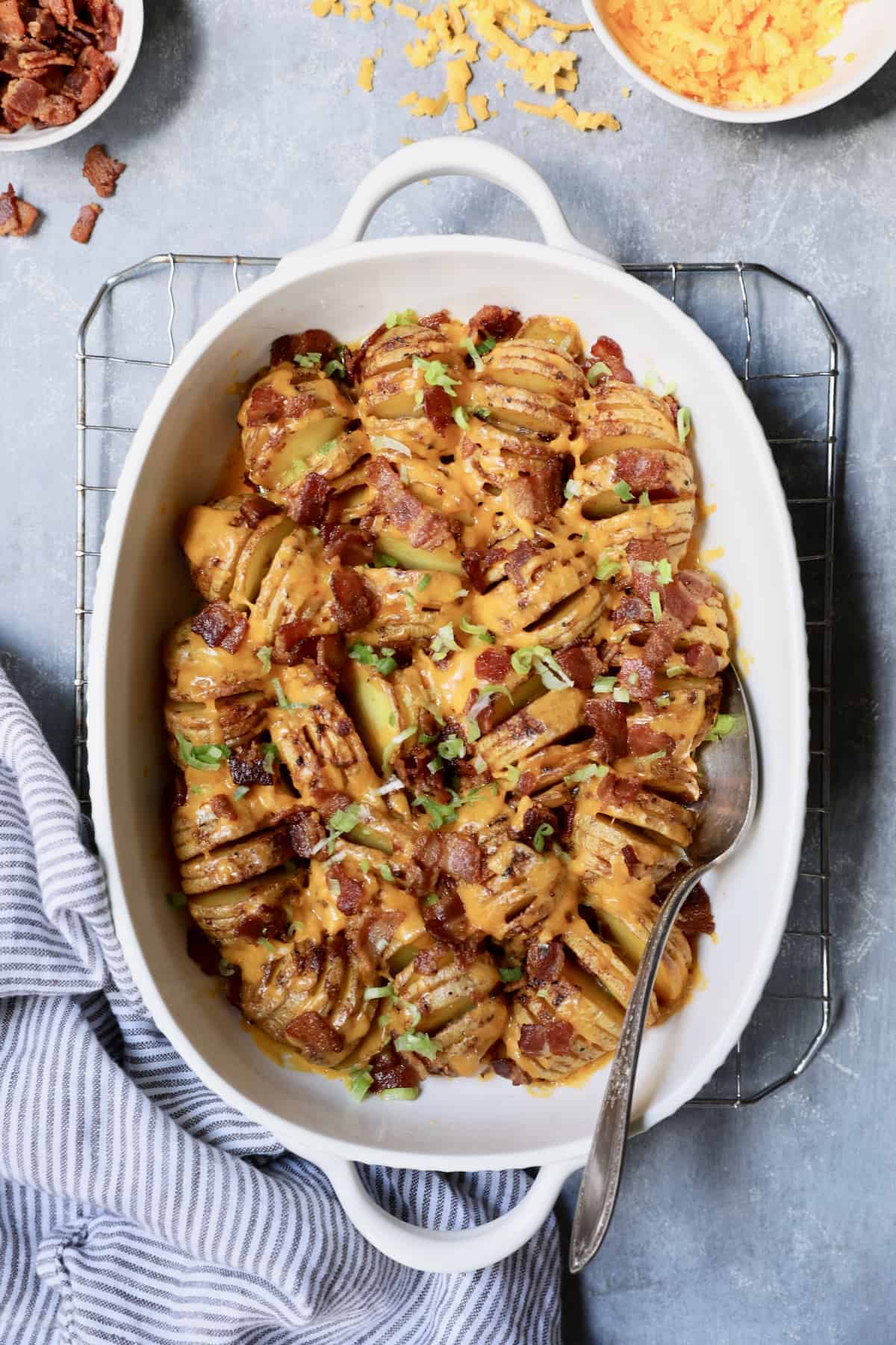 Photo of Baby Hasselback Potato Bake with Cheddar and Bacon in white baking dish with serving spoon.