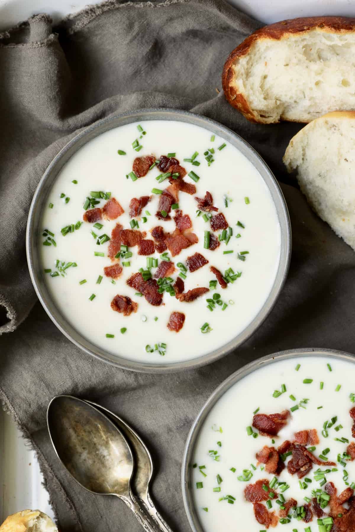 Close-up photo of Potato Leek Soup with White Cheddar in gray bowls garnished with bacon and chives.