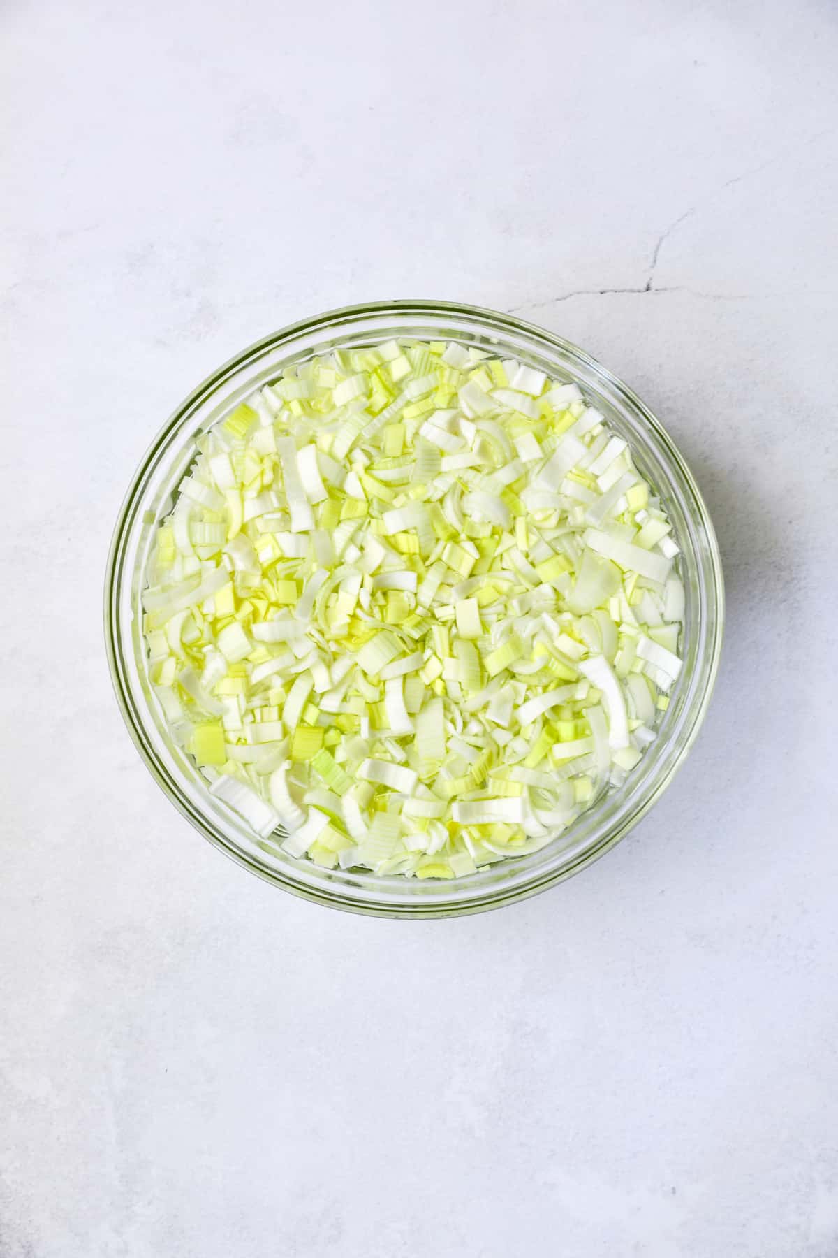 Photo of sliced leeks in glass bowl immersed in water.
