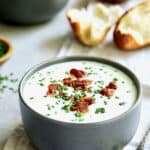 Potato and Leek Soup with White Cheddar - Straight-on shot of soup in gray bowl with broken bread in the background
