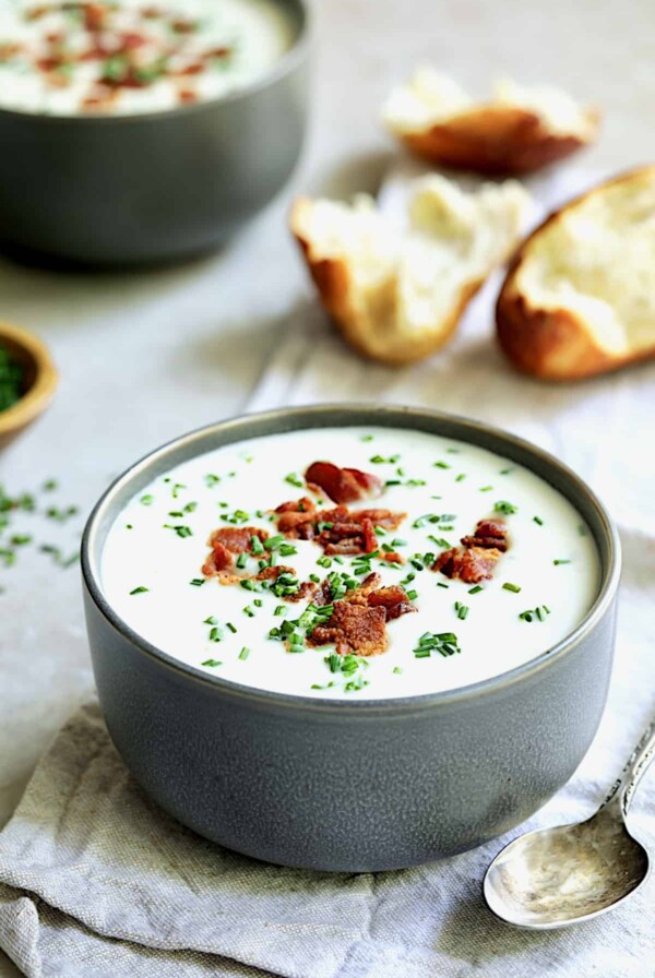 Potato and Leek Soup with White Cheddar - Straight-on shot of soup in gray bowl with broken bread in the background