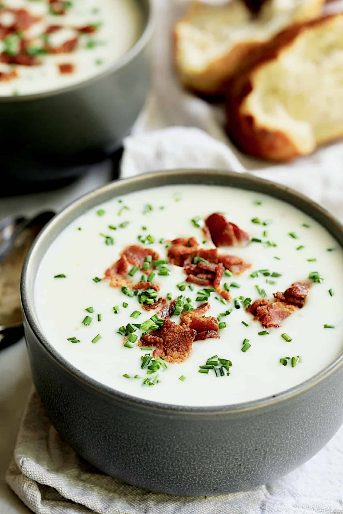 Close-up photo of Potato and Leek Soup with White Cheddar in gray bowl garnished with bacon and chives.