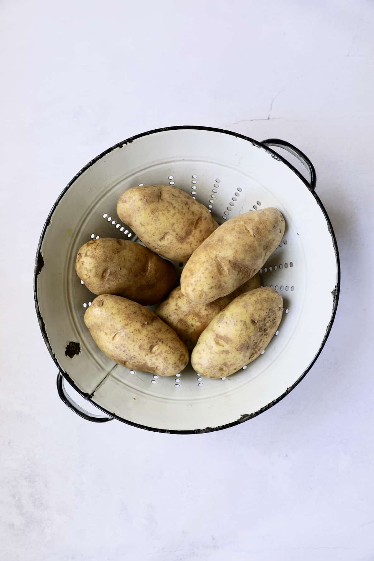 Photo of Russet potatoes in white distressed colander.