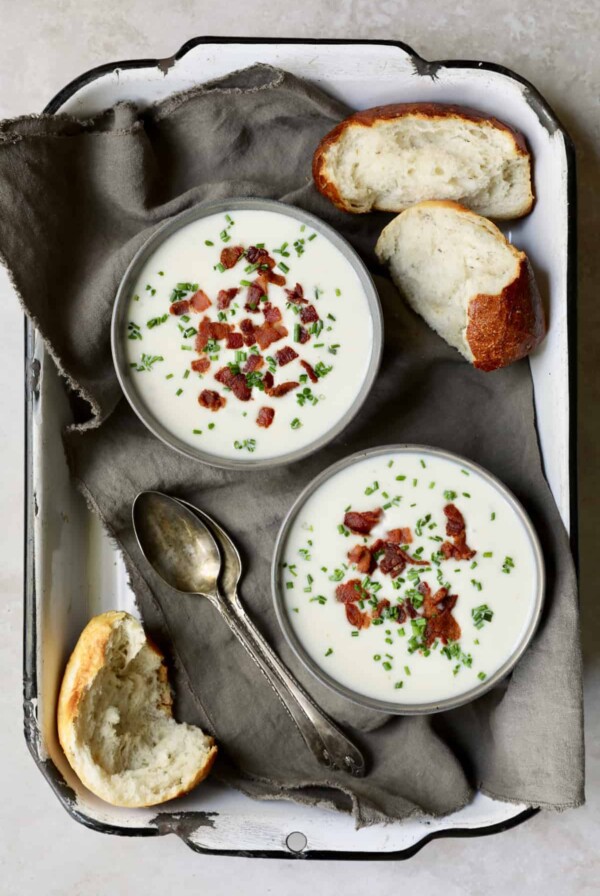 Potato and Leek Soup with White Cheddar - Overhead hero shot of two bowls of soup in white distressed tray with bread