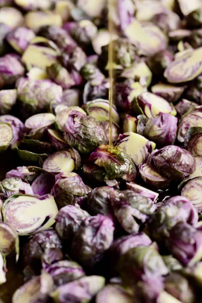Photo of oil being drizzled over purple Brussels sprouts.