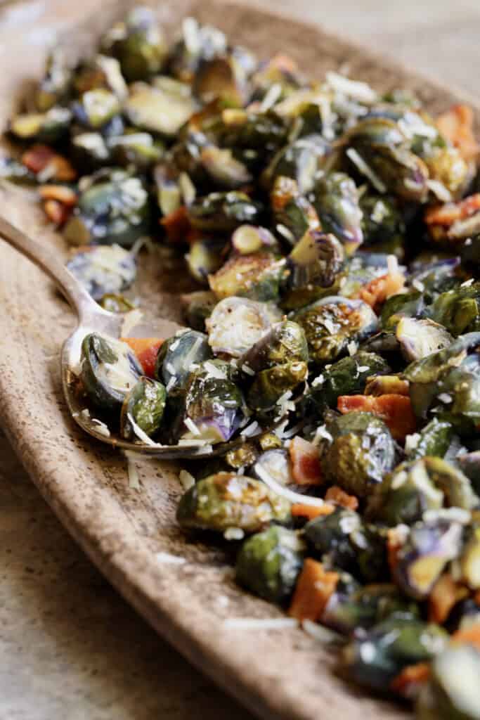 Photo of Roasted Purple Brussels Sprouts with Bacon and Parmesan on brown platter with serving spoon.
