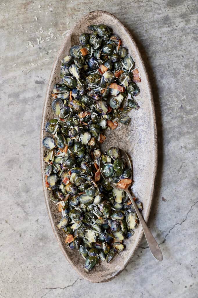 Photo of Roasted Purple Brussels Sprouts with Bacon and Parmesan on oval platter with serving spoon.