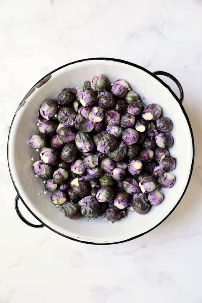 Photo of purple Brussels sprouts in white colander.