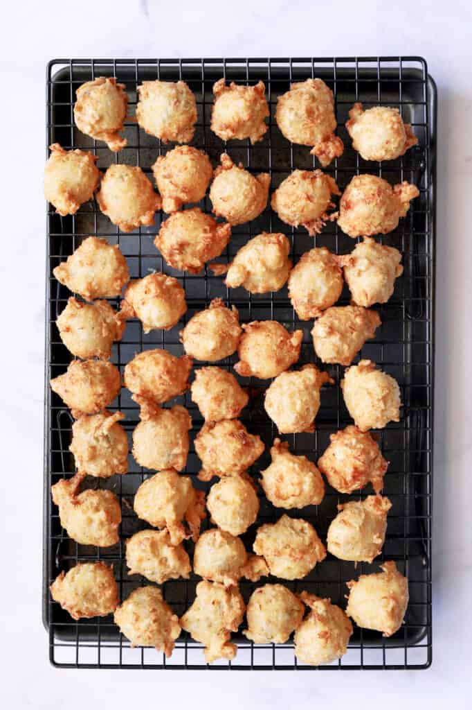 Photo of fried Crab and Artichoke Beignets on cooling rack set over a rimmed sheet pan.