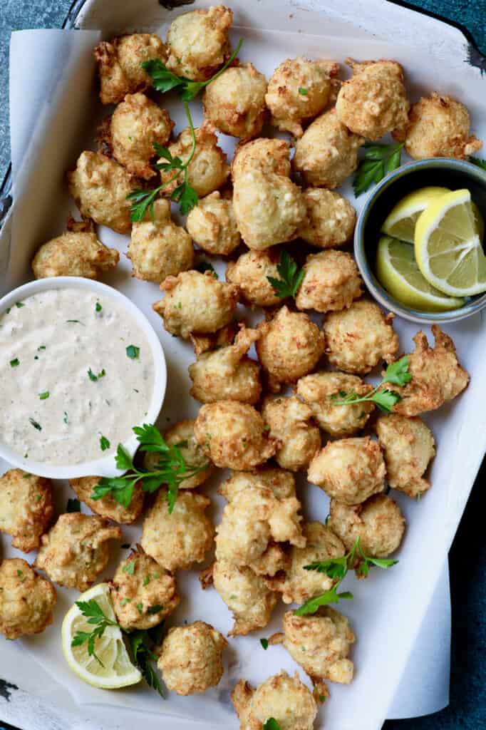 Photo of Crab and Artichoke Beignets with Jalapeno Remoulade in white pan with lemon wedges.