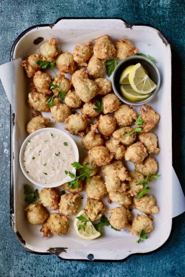 Crab and Artichoke Beignets with Jalapeno Remoulade - Overhead hero shot of beignets in white distressed pan garnished with parsley and lemon