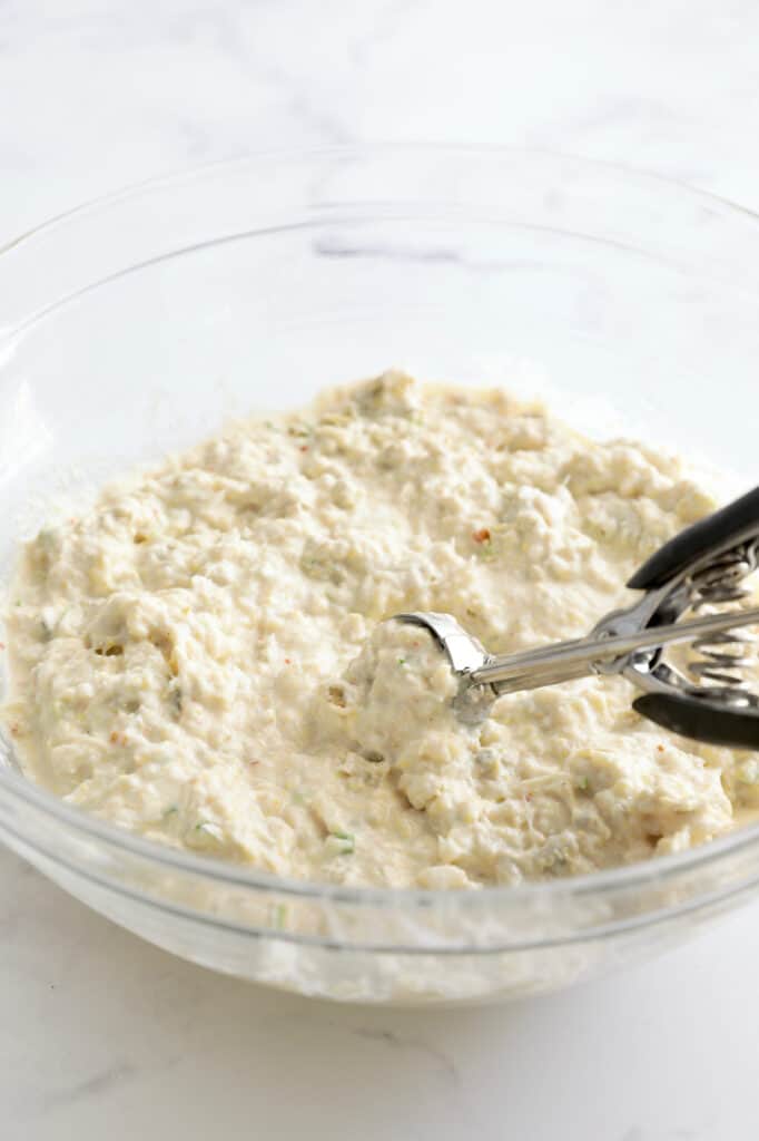 Photo of beignet batter being scooped out from glass bowl.