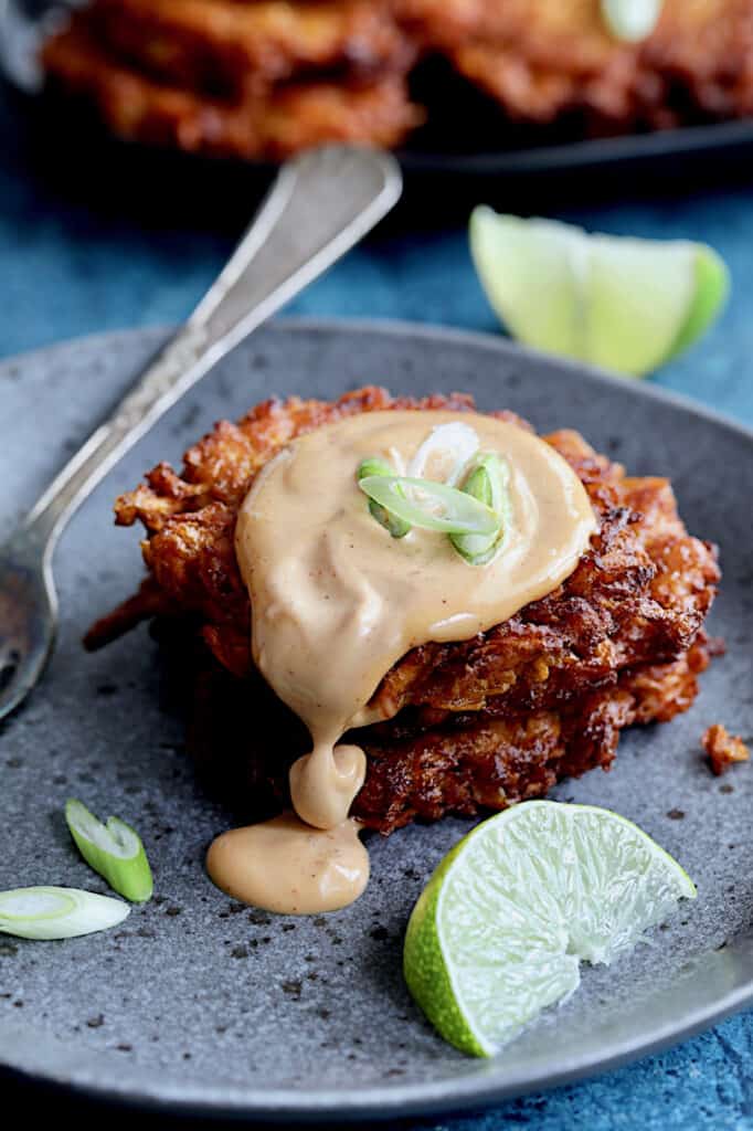 Close-up photo of two Korean Sweet Potato Latkes with Gochujang Mayonnaise on gray plate with mayonnaise dripping down.