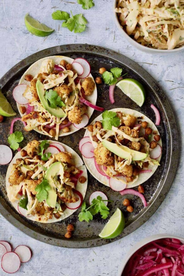 Cauliflower and Chickpea Tacos with Chipotle Lime Slaw - Overhead shot of three tacos with garnishes on light blue background