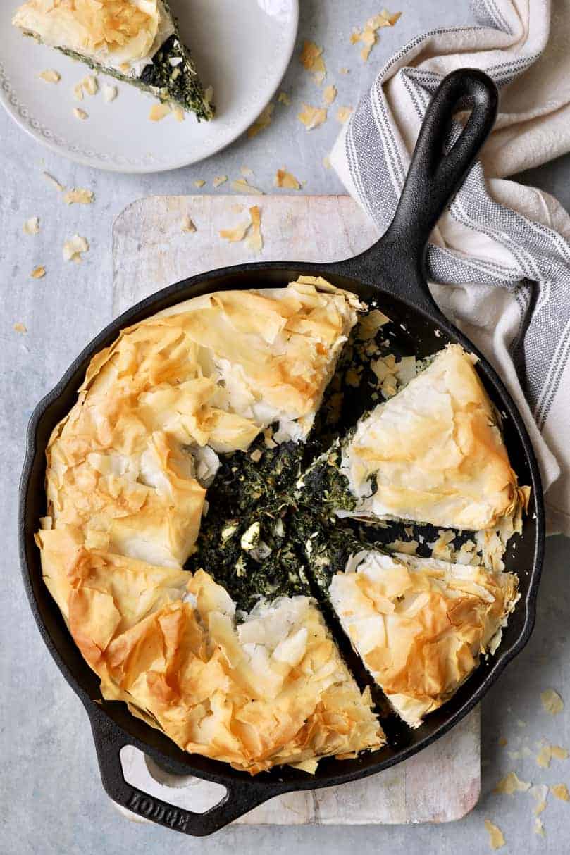 Photo of Skillet Spanakopita (Greek Spinach and Feta Pie) cast iron skillet with gray striped towel.