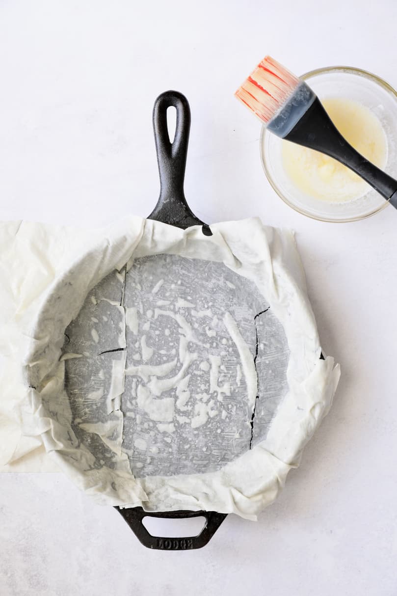 Photo of one piece of phyllo dough being buttered in cast iron skillet.