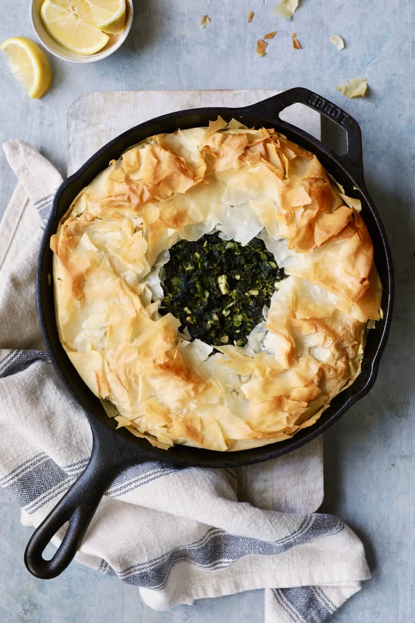 Photo of Skillet Spanakopita (Greek Spinach and Feta Pie) on cutting board after being baked with gray striped towel.
