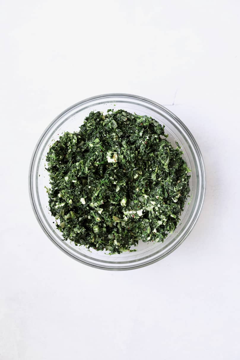 Photo of ingredients for spanakopita combined in glass bowl.