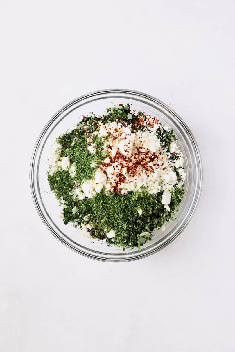 Photo of ingredients for spanakopita combined in glass bowl.