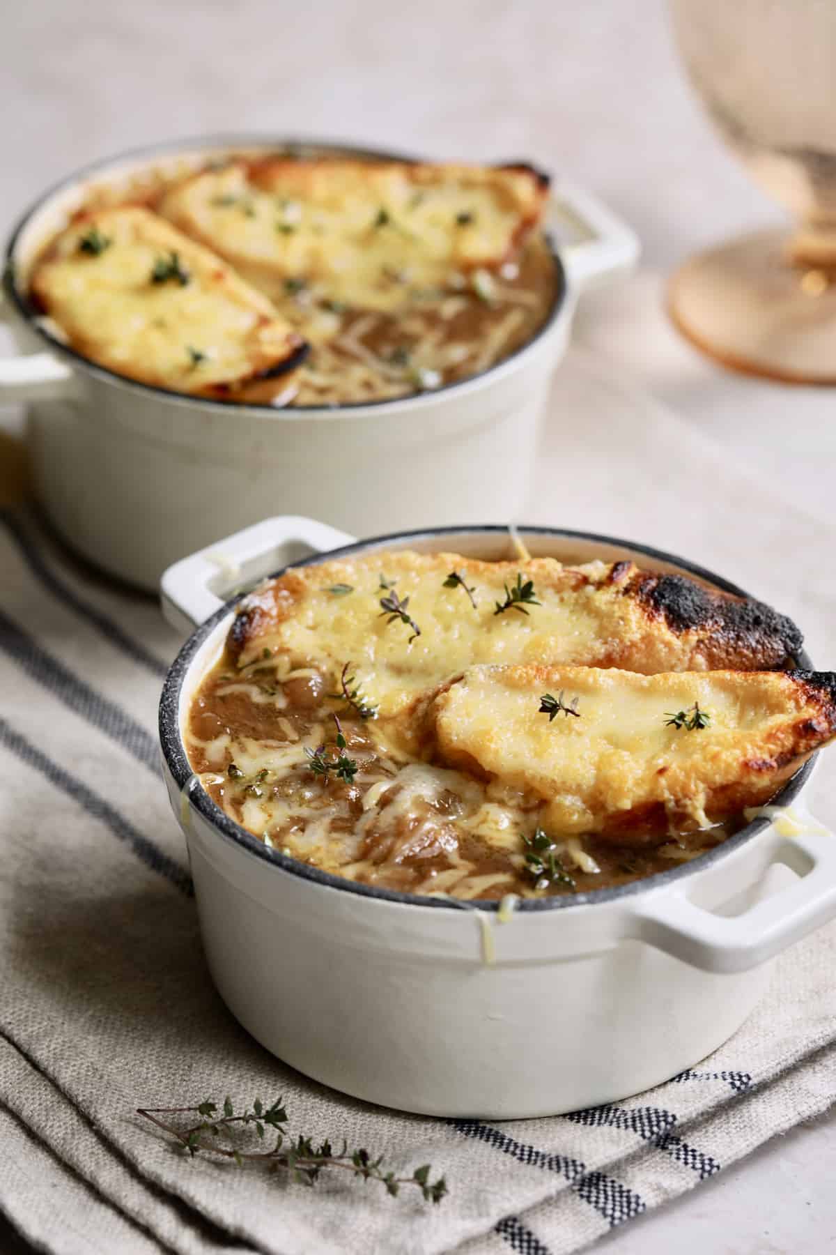 Photo of French Onion Soup for Two on black striped napkin garnished with the bread and thyme leaves.