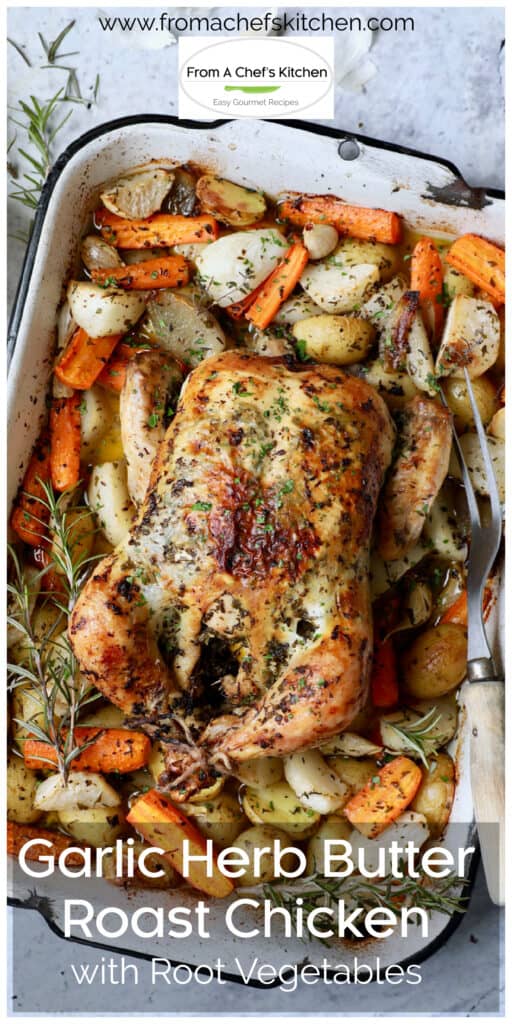 Garlic Herb Butter Roast Chicken with root vegetables in white roasting pan with meat fork.