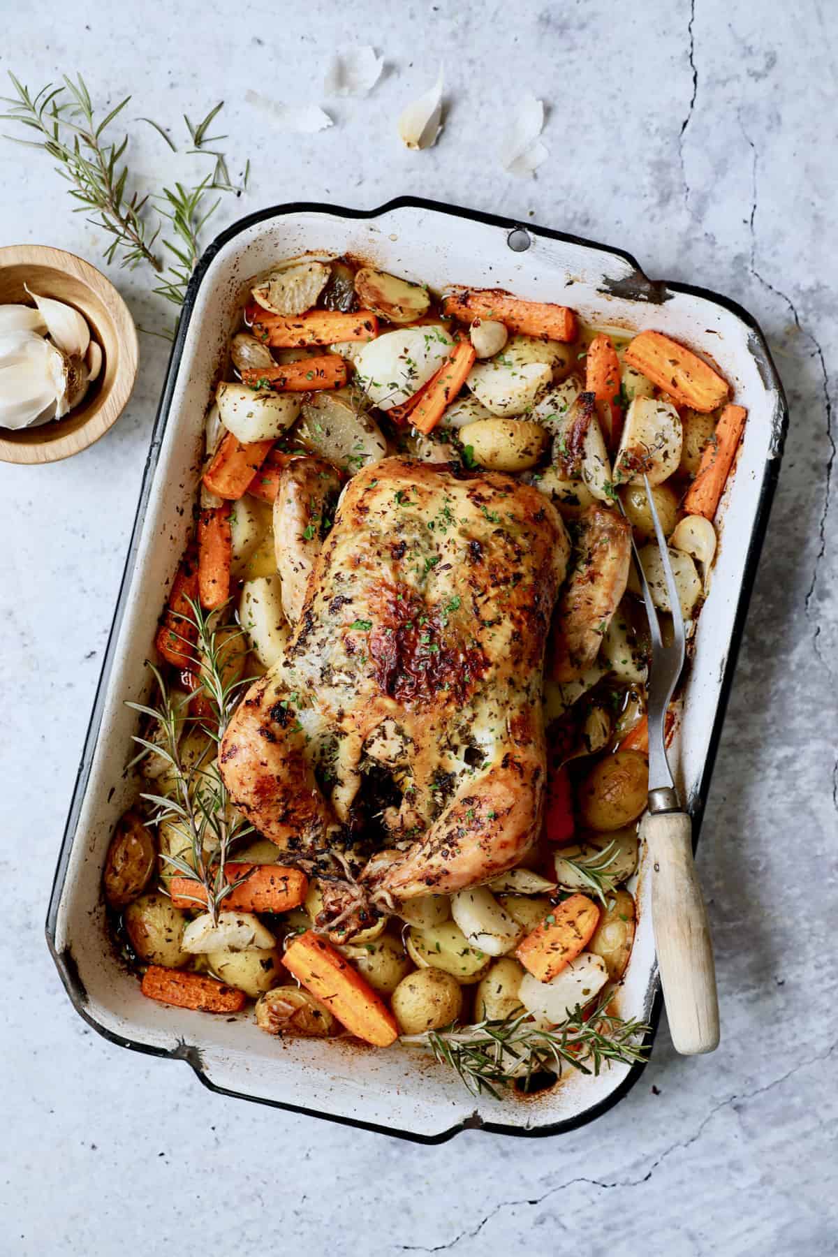 Photo of Garlic Herb Butter Roast Chicken with Root Vegetables in white distressed roasting pan.