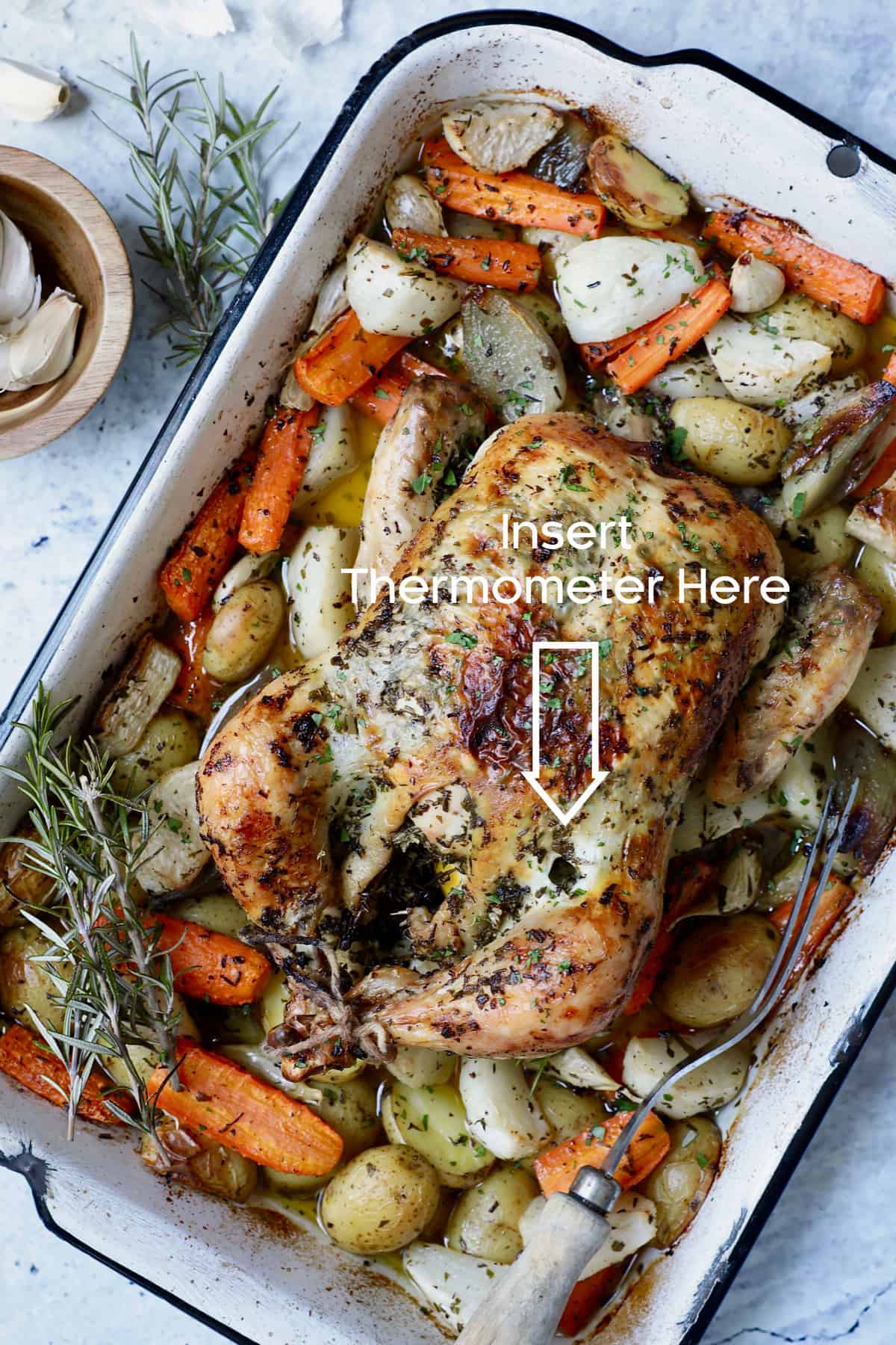 Photo of Garlic Herb Roast Chicken with Root Vegetables garnished with rosemary showing where to test for doneness.