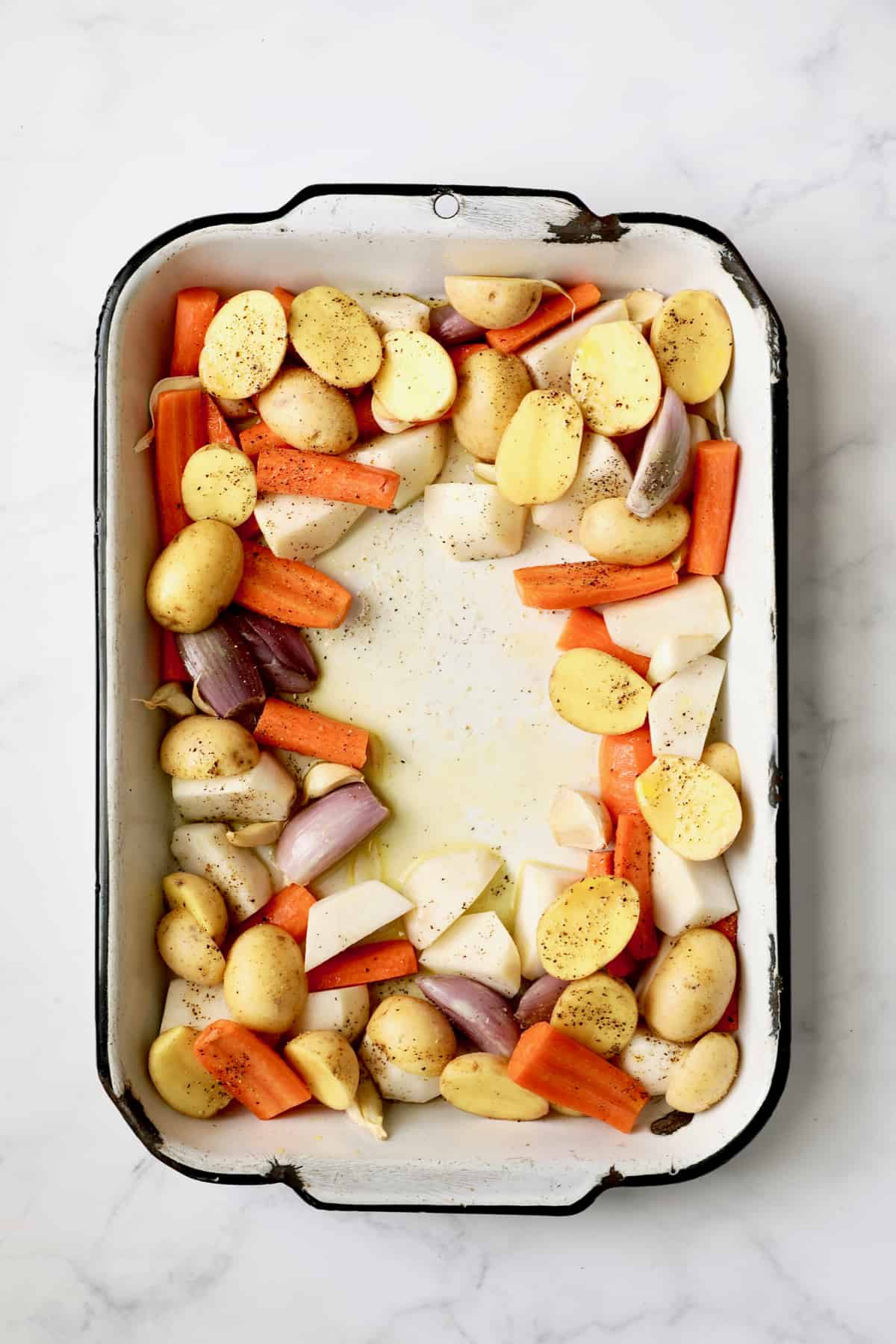 Photo of uncooked root vegetables in white roasting pan.