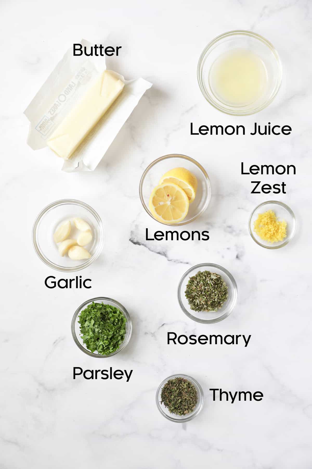 Ingredients for garlic herb butter in glass bowls on marble background.