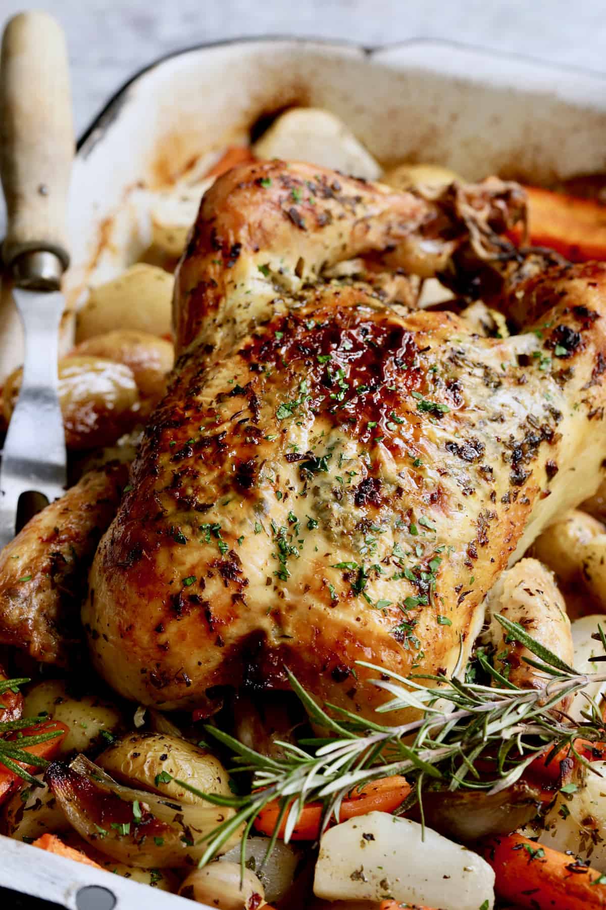Photo of Garlic Herb Butter Roast Chicken with Root Vegetables with meat fork nearby.