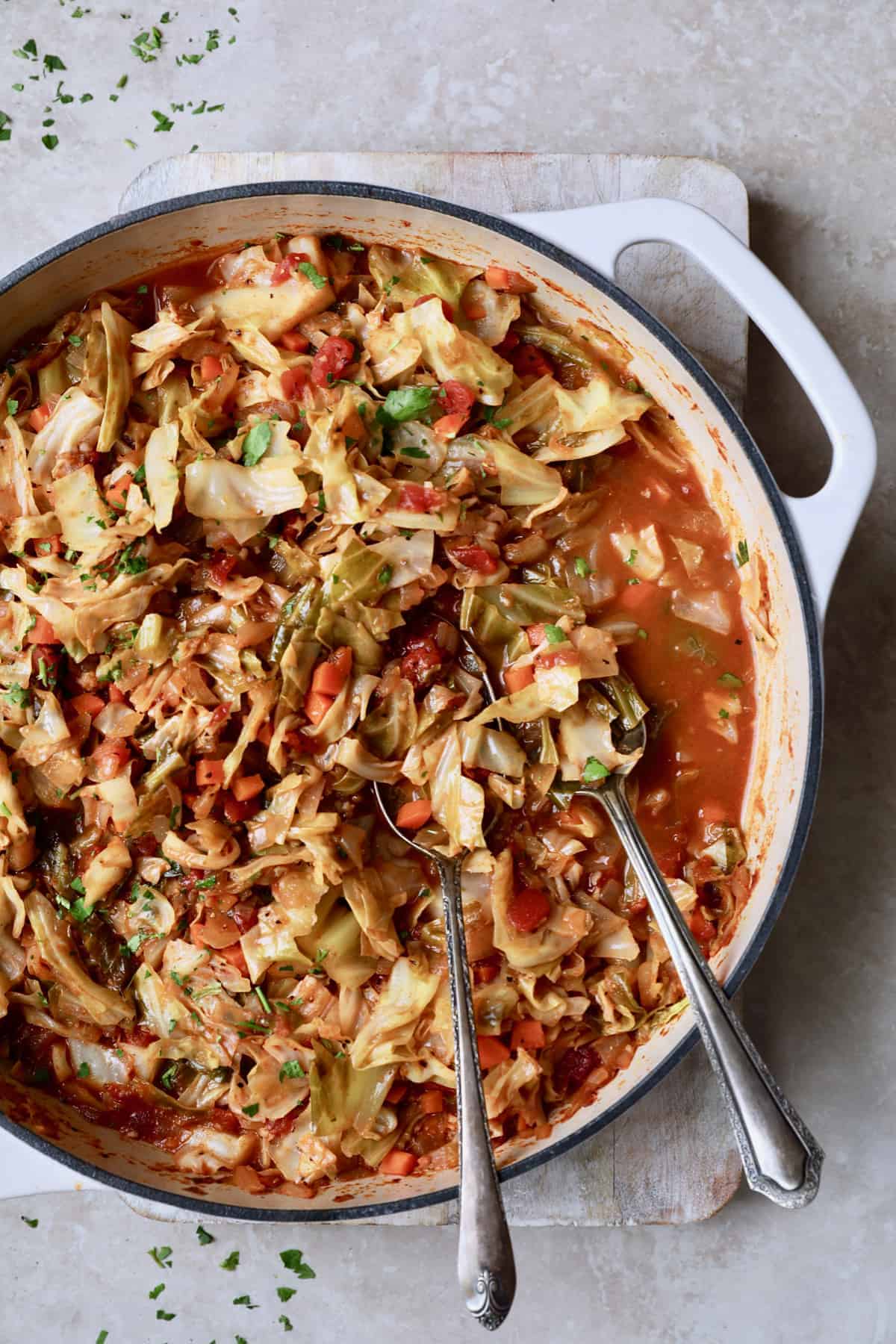 Photo of Polish Stewed Cabbage (Kapusta) in white cast iron skillet with utensils.