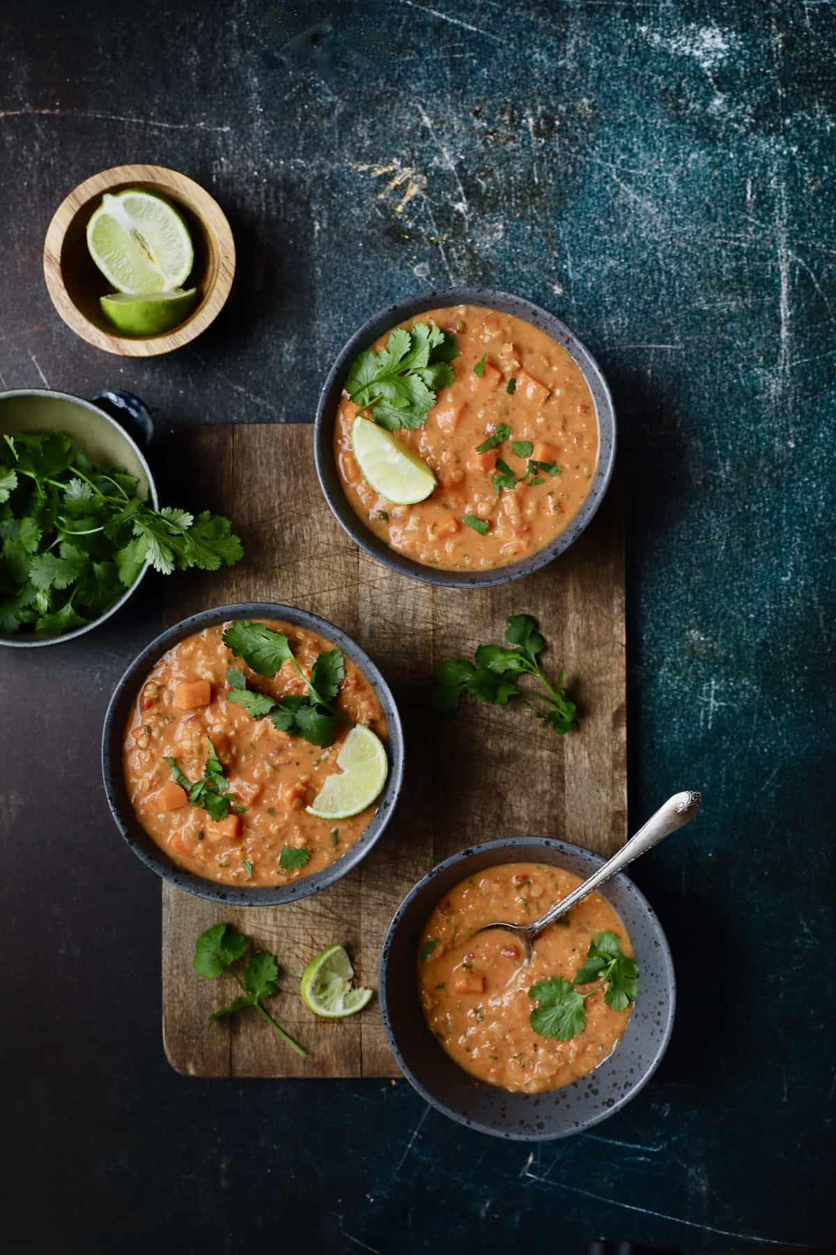 Photo of Thai Red Curry Sweet Potato and Lentil Soup garnished with lime and cilantro on blue distressed background.