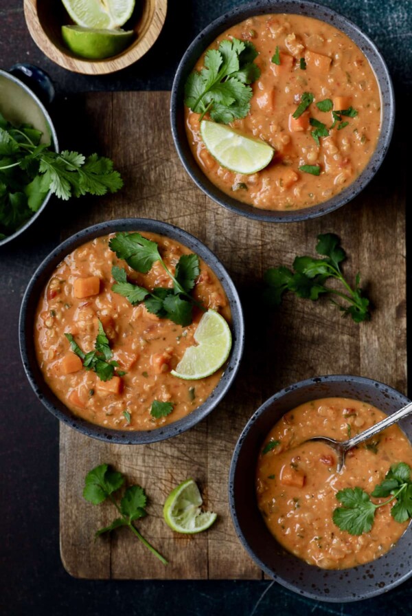 Photo of Thai Red Curry Sweet Potato and Lentil Soup in three gray bowls on wood surface.
