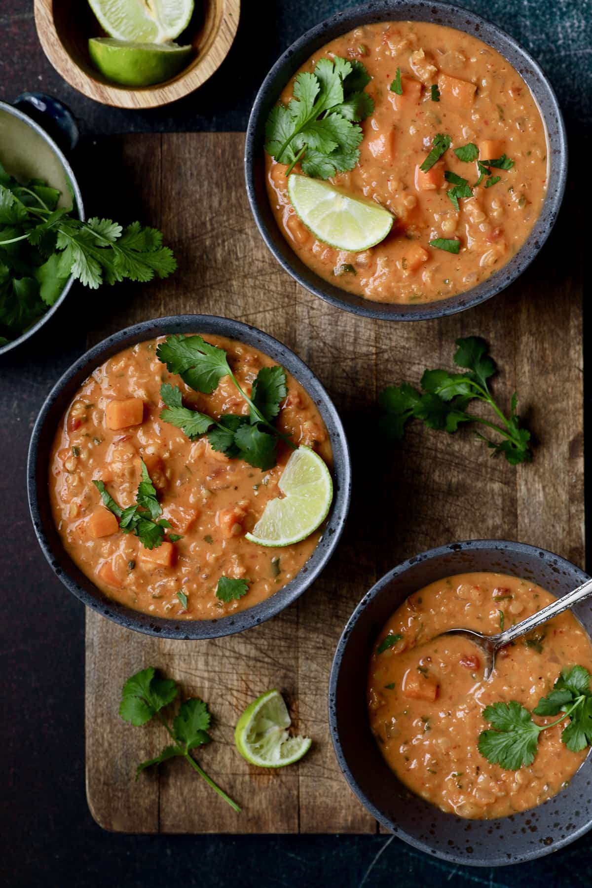 Photo of Thai Red Curry Sweet Potato and Lentil Soup in three gray bowls on wood surface.