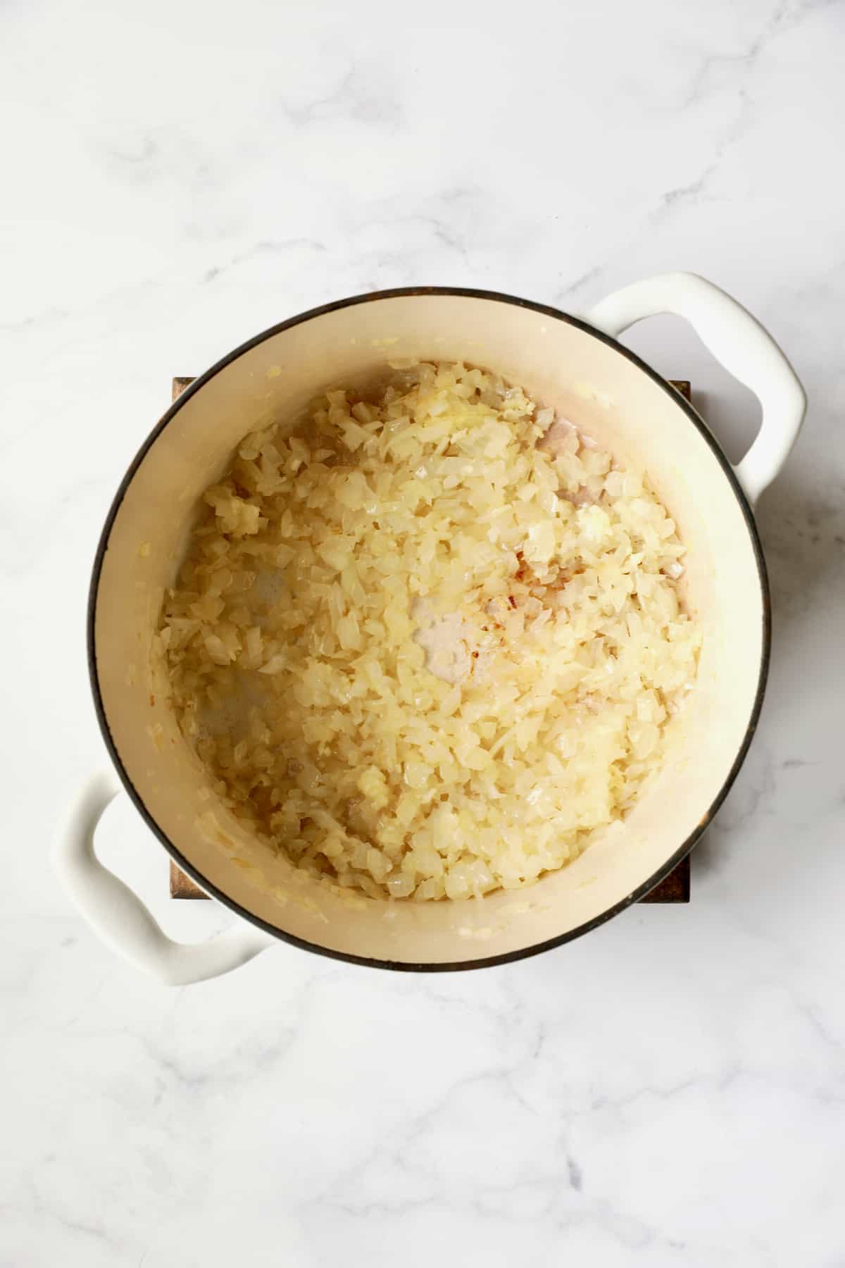 Process photo of onions cooking in white Dutch oven.
