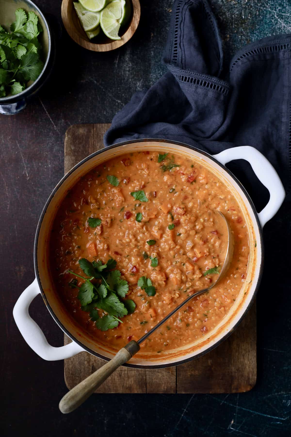 Photo of Thai Red Curry Sweet Potato and Lentil Soup on wood cutting board in white Dutch oven.