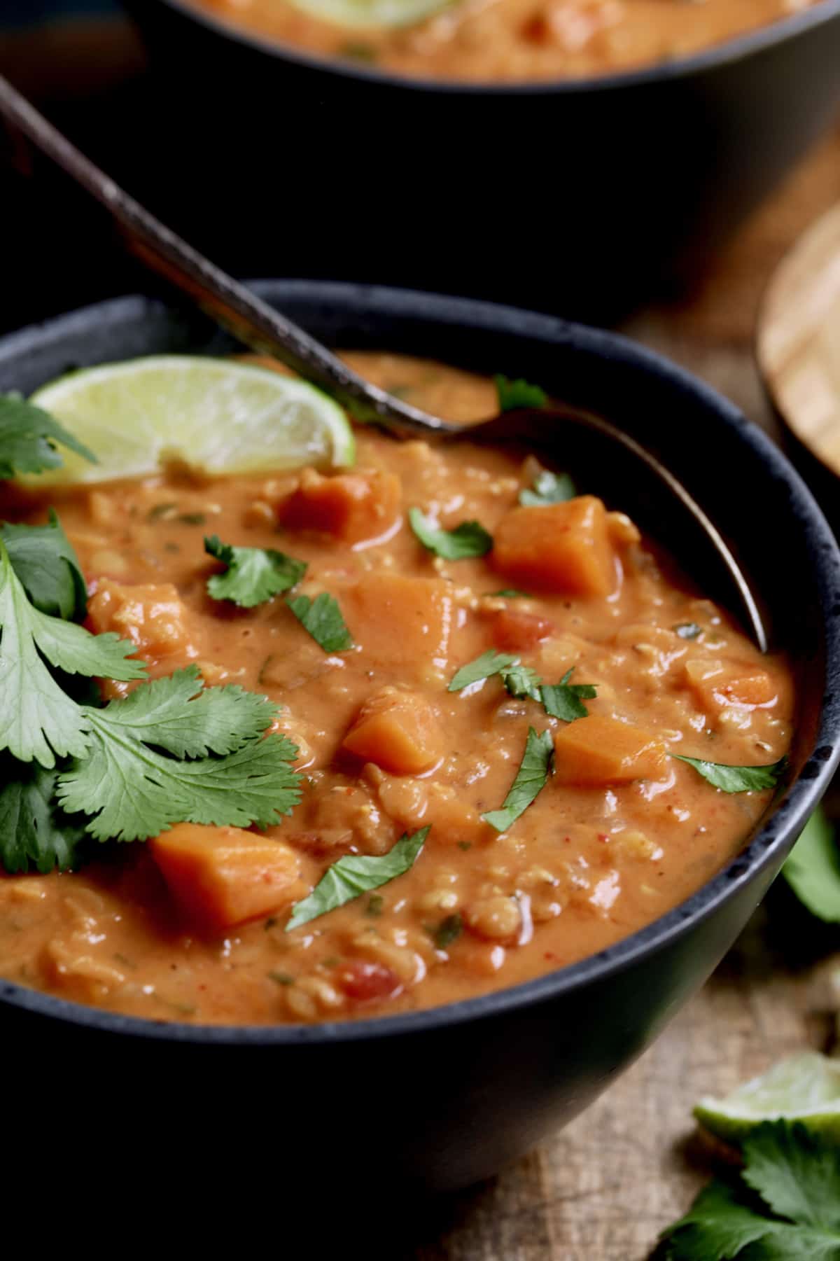 Close-up photo of Thai Red Curry Sweet Potato and Lentil Soup in gray bowl garnished with lime and cilantro.