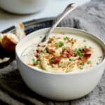 Photo of Cauliflower Potato Soup with Smoked Gouda in white bowl with soup spoon.