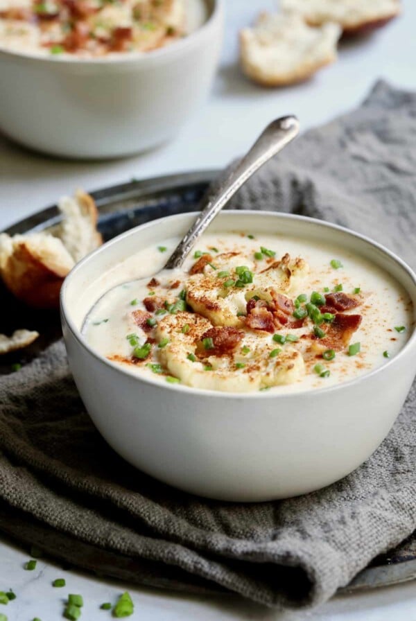 Photo of Cauliflower Potato Soup with Smoked Gouda in white bowl with soup spoon.