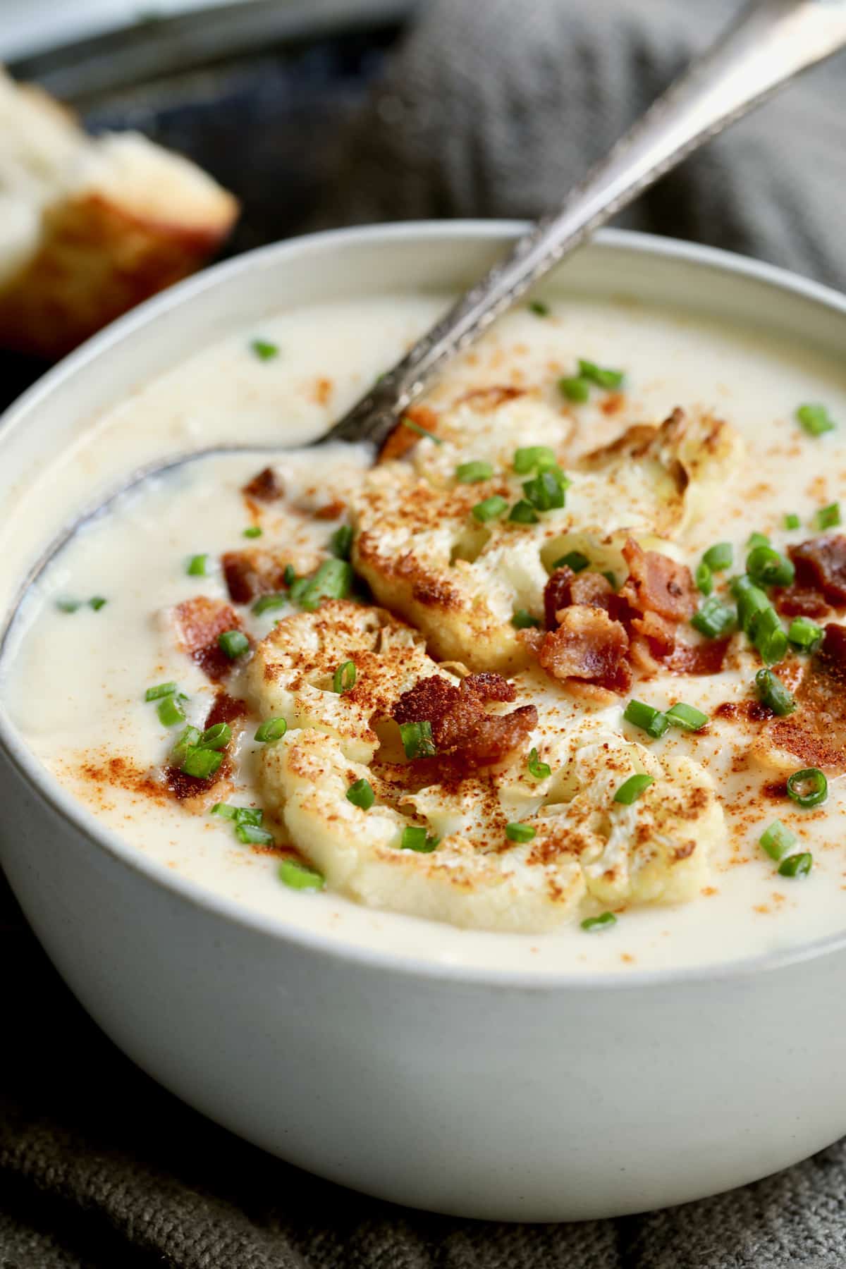Cauliflower Potato Soup with Smoked Gouda in white bowl garnished with bacon and chives.