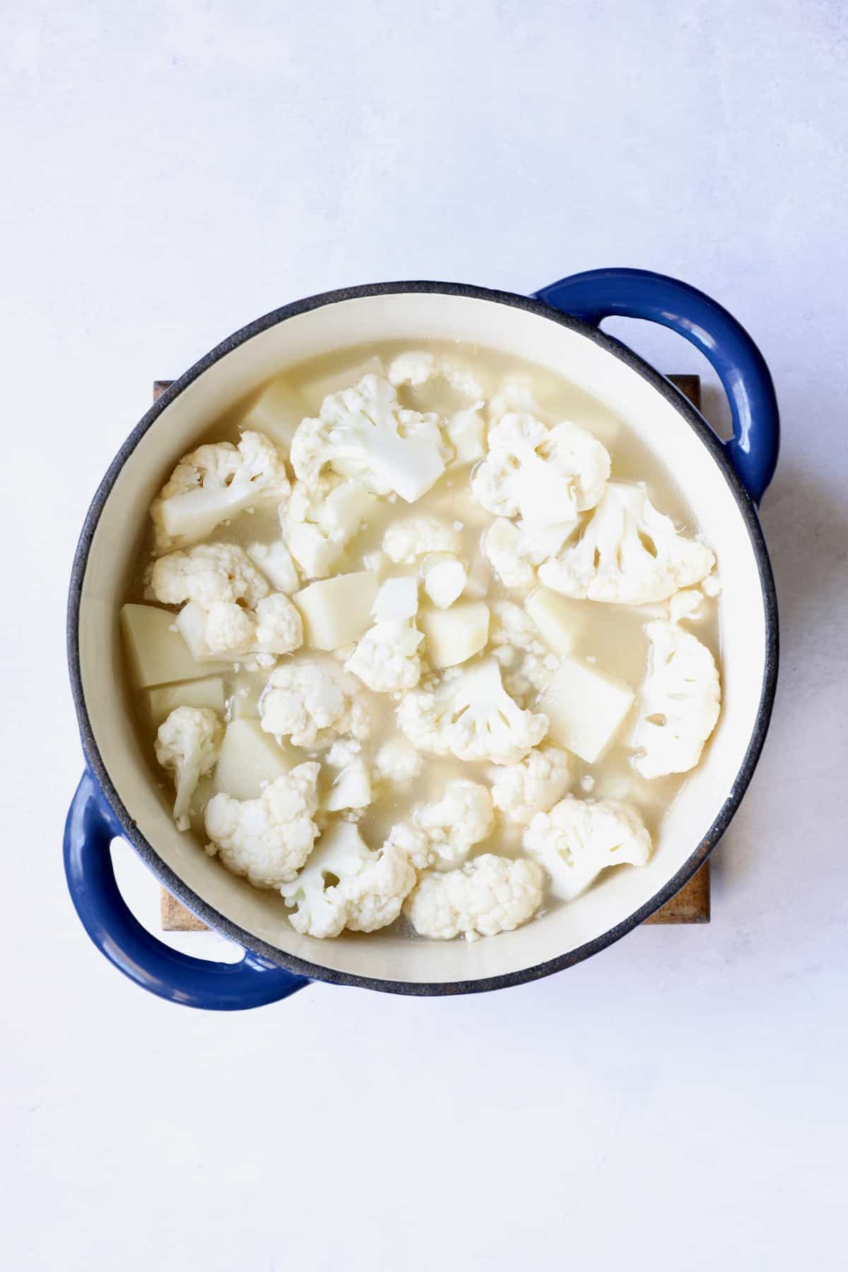 Potatoes and cauliflower cooking in the broth in blue Dutch oven.