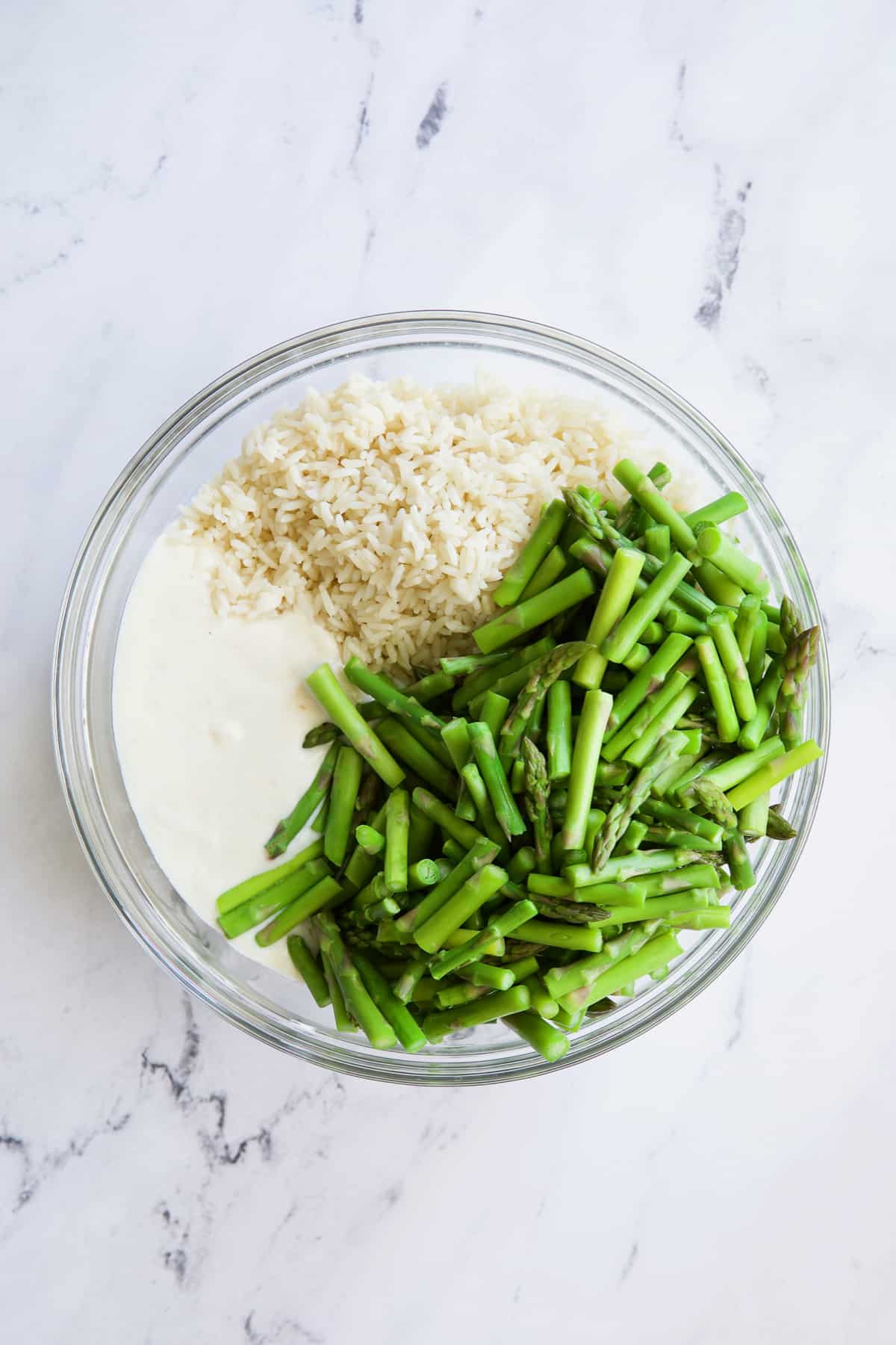 Photo of cream sauce, rice and blanched asparagus in glass bowl.