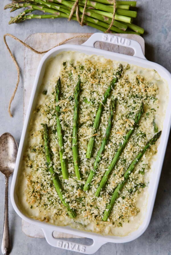 Photo of Creamy Asparagus and Rice Casserole in white baking dish with serving spoon and bunch of asparagus.