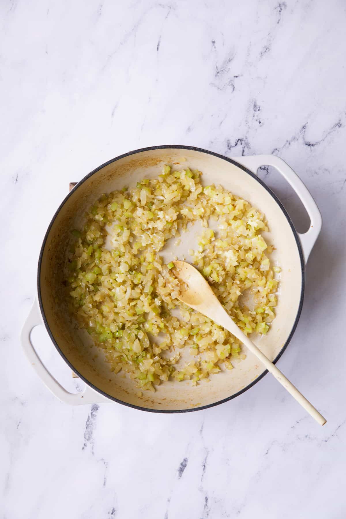 Photo of cooked onion and celery in white cast iron skillet.