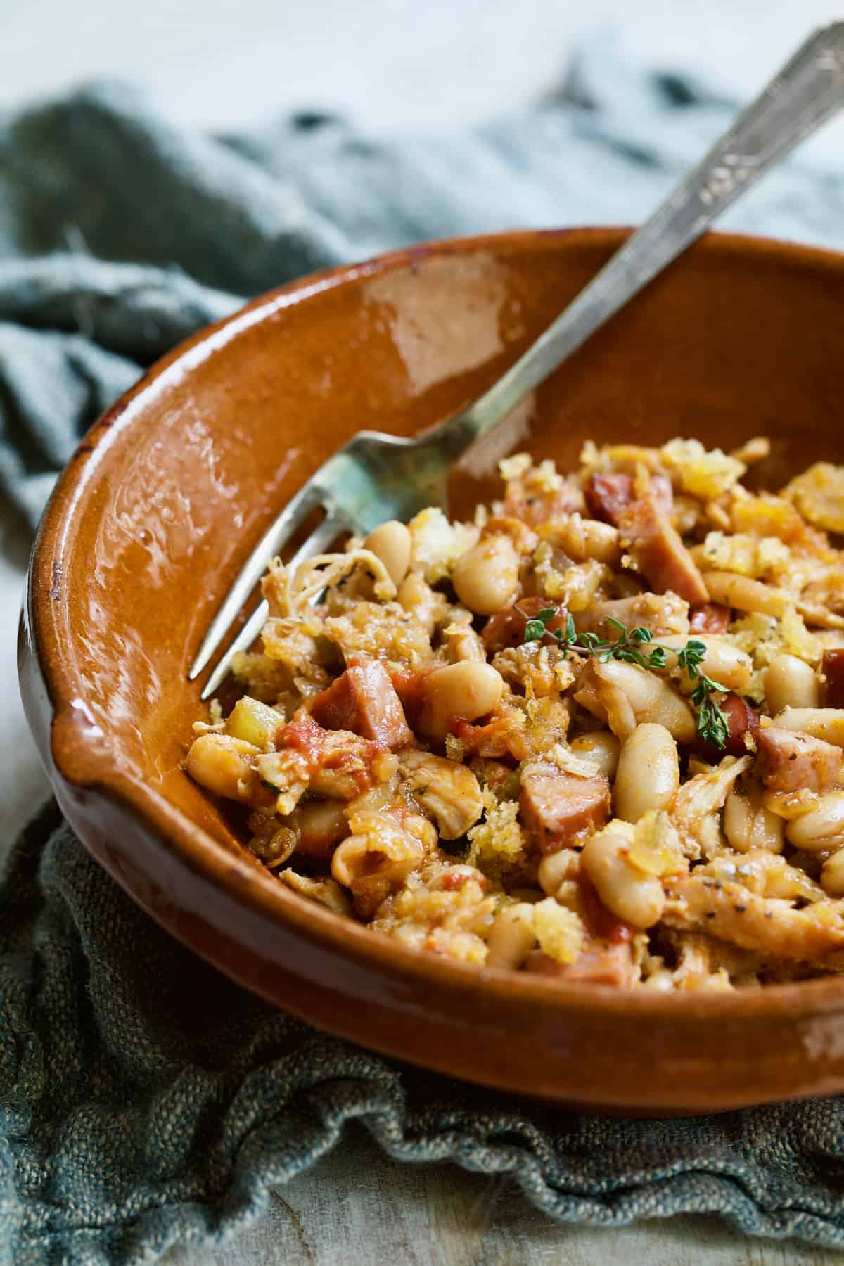 Photo of one serving of Easy Weeknight Chicken and Sausage Cassoulet in red clay bowl.