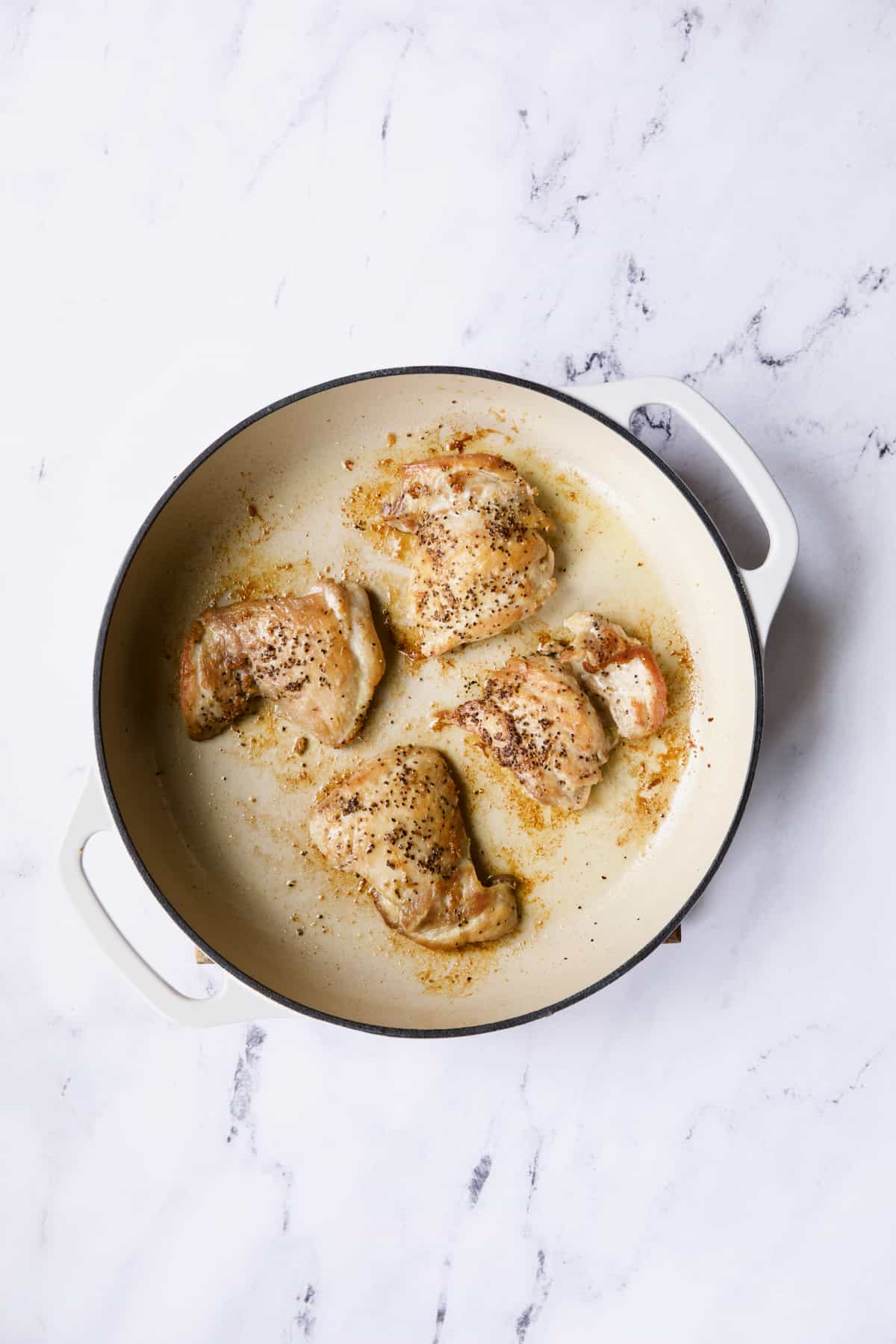 Photo of four boneless skinless chicken thighs in white cast iron skillet.
