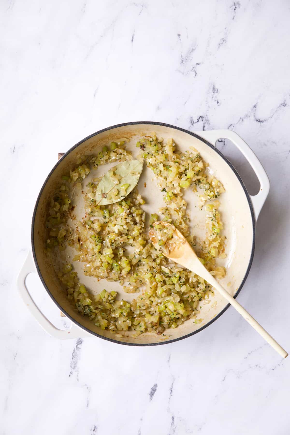 Photo of sauteed onion, celery and spices in white cast iron skillet.
