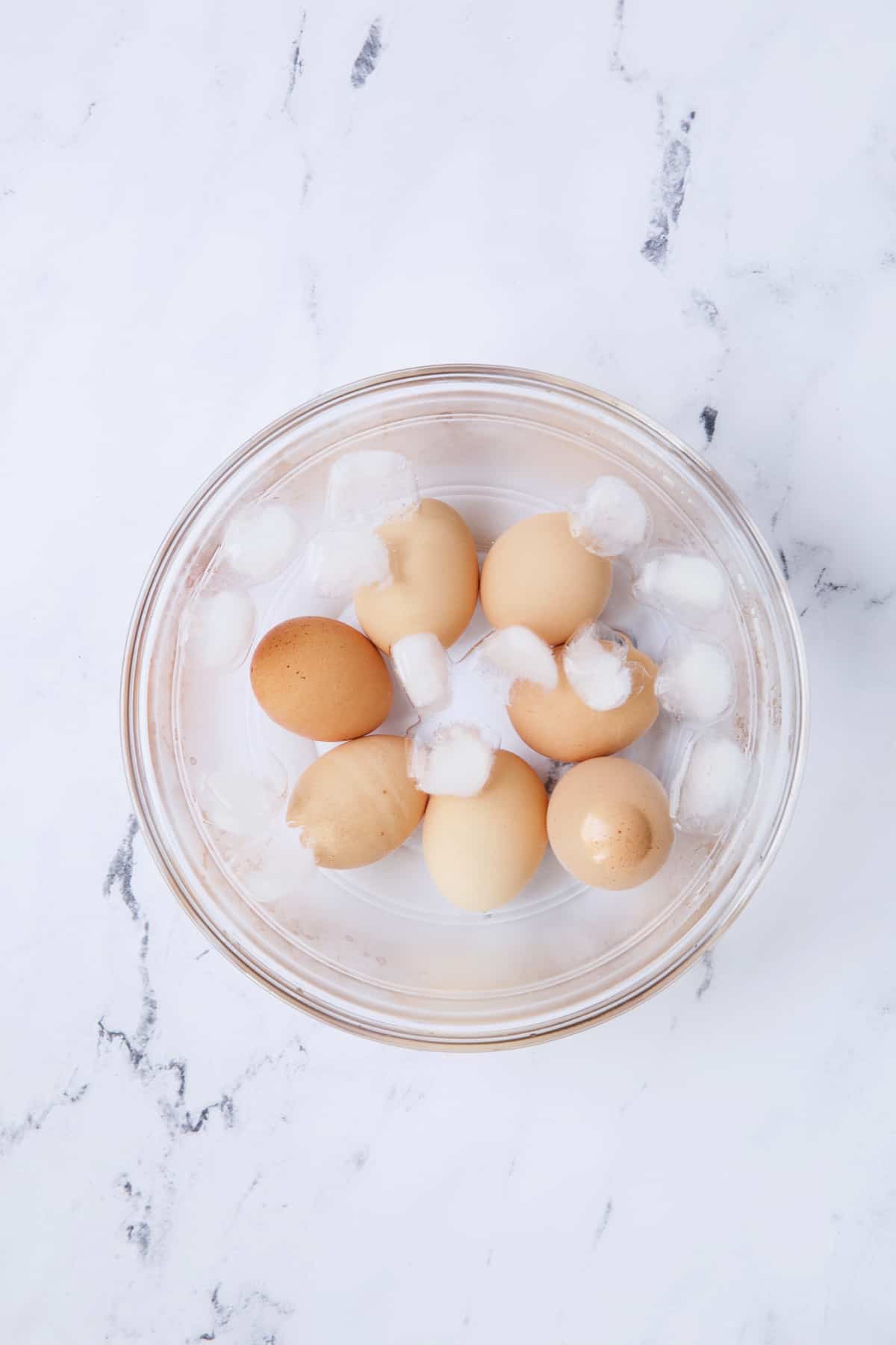 Photo of seven eggs in ice bath in glass bowl.
